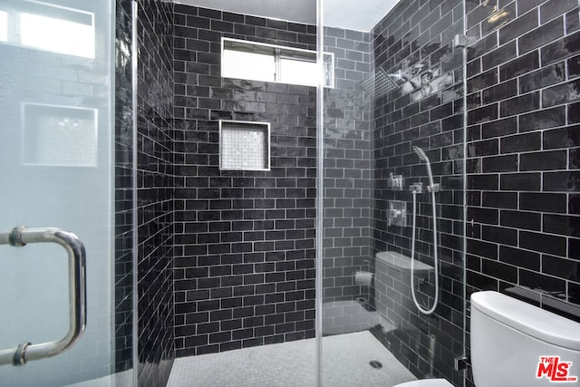 bathroom with toilet, tile walls, and a shower with shower door