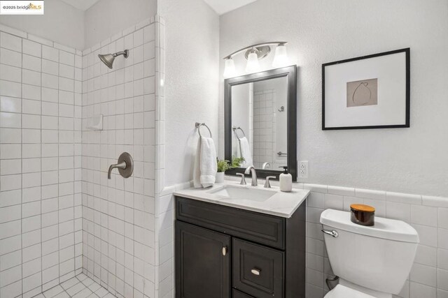 bathroom with vanity, tiled shower, tile walls, and toilet