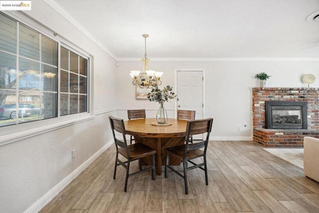 dining room featuring ornamental molding, a fireplace, a chandelier, and light wood-type flooring