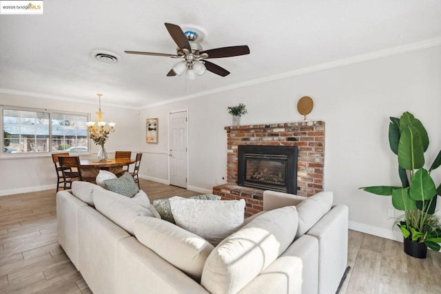 living room featuring crown molding, a brick fireplace, ceiling fan with notable chandelier, and light hardwood / wood-style flooring