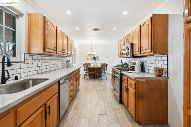 kitchen with sink, ornamental molding, appliances with stainless steel finishes, pendant lighting, and backsplash