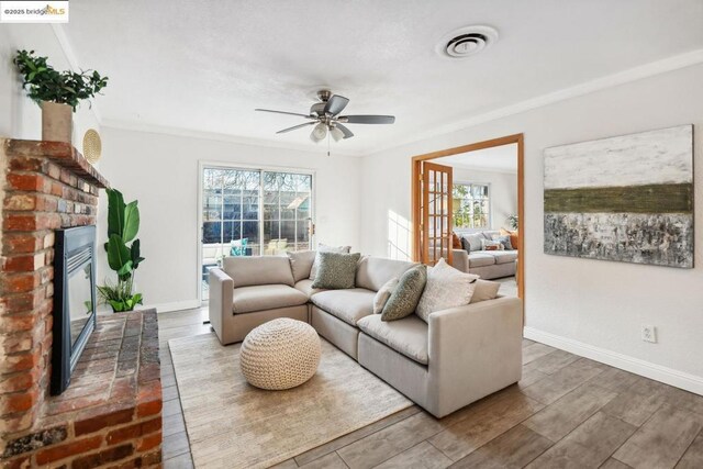 living room featuring hardwood / wood-style flooring, ceiling fan, ornamental molding, and a brick fireplace