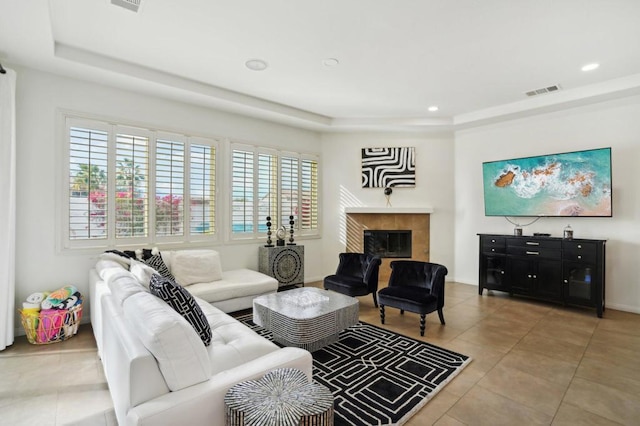 living room with a tile fireplace, tile patterned floors, and a tray ceiling