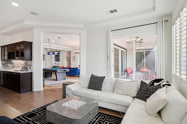 tiled living room featuring pool table, plenty of natural light, a raised ceiling, and a chandelier