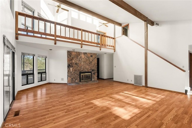 unfurnished living room featuring hardwood / wood-style floors, beam ceiling, a fireplace, and ceiling fan