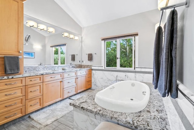 bathroom featuring vanity, lofted ceiling, and a bath