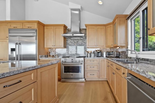 kitchen featuring lofted ceiling, sink, premium appliances, light stone counters, and wall chimney range hood