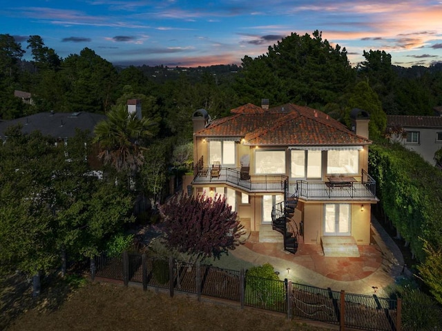 back house at dusk featuring a balcony and a patio area