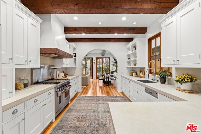 kitchen with sink, range with two ovens, custom range hood, white cabinets, and light wood-type flooring