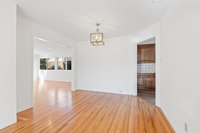 spare room featuring a notable chandelier and light wood-type flooring