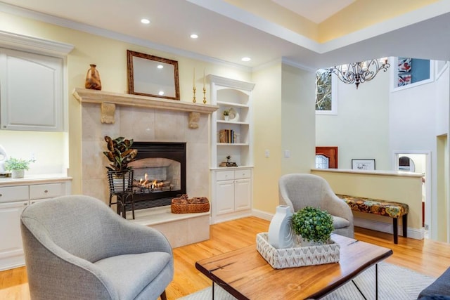 living area featuring a tiled fireplace, ornamental molding, built in features, and light hardwood / wood-style floors