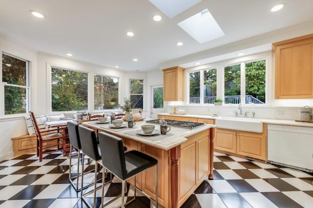 kitchen with sink, dishwasher, stainless steel gas cooktop, a kitchen island, and light brown cabinetry