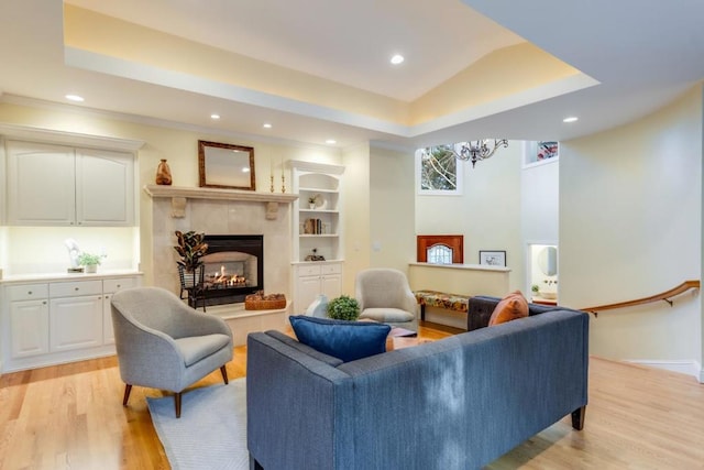 living room featuring built in features, light hardwood / wood-style floors, a tile fireplace, and a raised ceiling