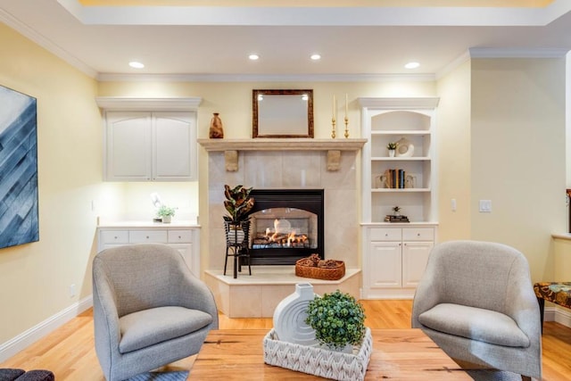 living area with built in features, ornamental molding, light hardwood / wood-style floors, and a tile fireplace