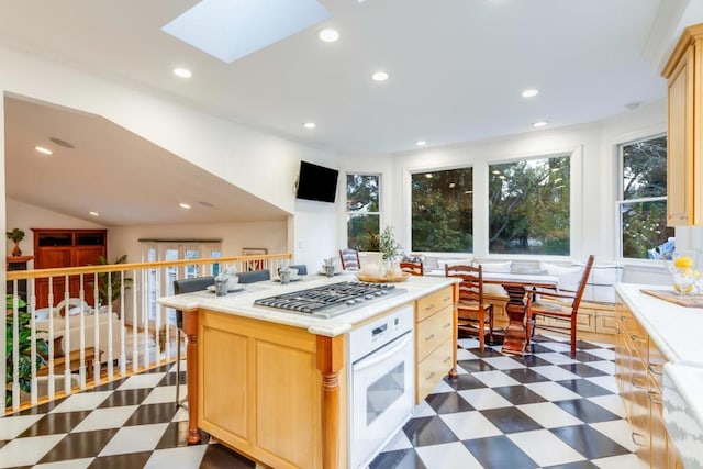 kitchen featuring white oven, a skylight, a center island, stainless steel gas cooktop, and light brown cabinetry