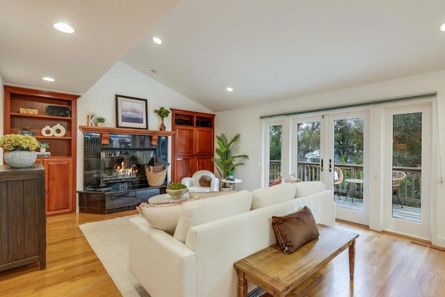 living room with a tiled fireplace, light hardwood / wood-style flooring, french doors, and vaulted ceiling