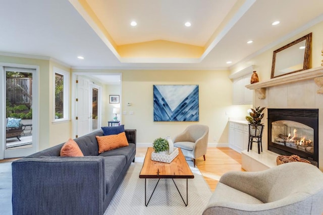 living room with ornamental molding, a tile fireplace, a raised ceiling, and light wood-type flooring