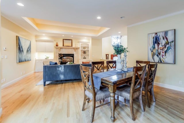 dining area with ornamental molding, light hardwood / wood-style flooring, built in features, and a raised ceiling