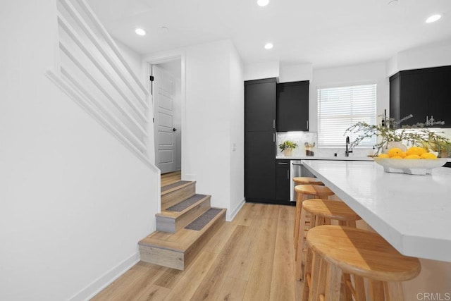 kitchen featuring sink, a breakfast bar area, light hardwood / wood-style flooring, dishwasher, and backsplash