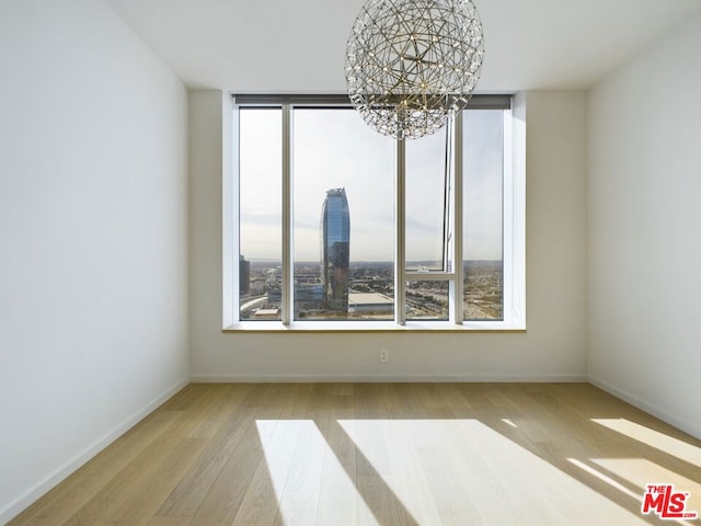 empty room with an inviting chandelier, a wealth of natural light, and light hardwood / wood-style floors