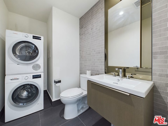 bathroom featuring tile patterned floors, stacked washer and clothes dryer, toilet, tile walls, and vanity