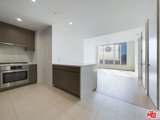 kitchen with dark brown cabinets, stainless steel oven, gas cooktop, and light tile patterned floors