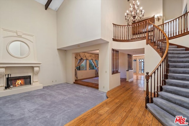 living room featuring an inviting chandelier, light wood-type flooring, beamed ceiling, and a high ceiling