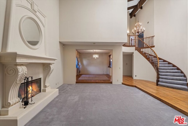 carpeted living room featuring a towering ceiling, a notable chandelier, and beam ceiling