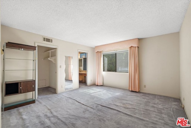 unfurnished bedroom with a walk in closet, ensuite bathroom, a closet, and a textured ceiling