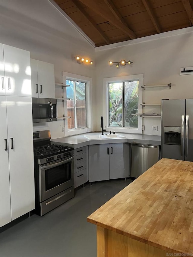 kitchen with lofted ceiling with beams, white cabinetry, sink, stainless steel appliances, and wooden ceiling