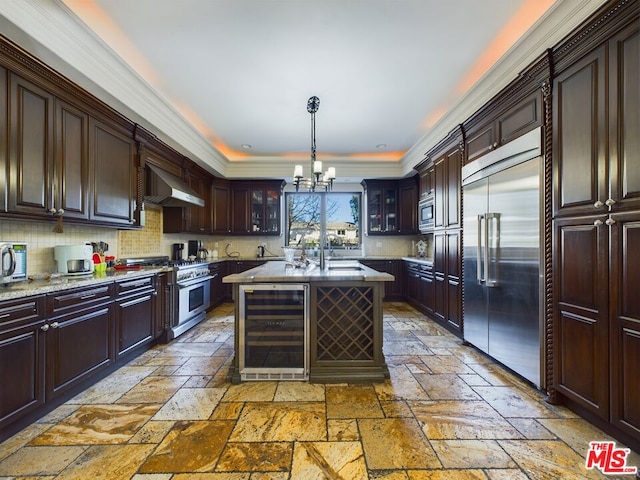 kitchen featuring a kitchen island, pendant lighting, wine cooler, built in appliances, and wall chimney exhaust hood