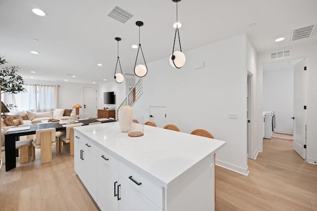 kitchen with white cabinetry, light wood-type flooring, hanging light fixtures, a center island, and washer and clothes dryer