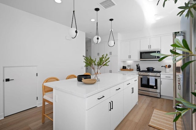 kitchen with white cabinetry, a kitchen island, pendant lighting, stainless steel appliances, and light hardwood / wood-style floors