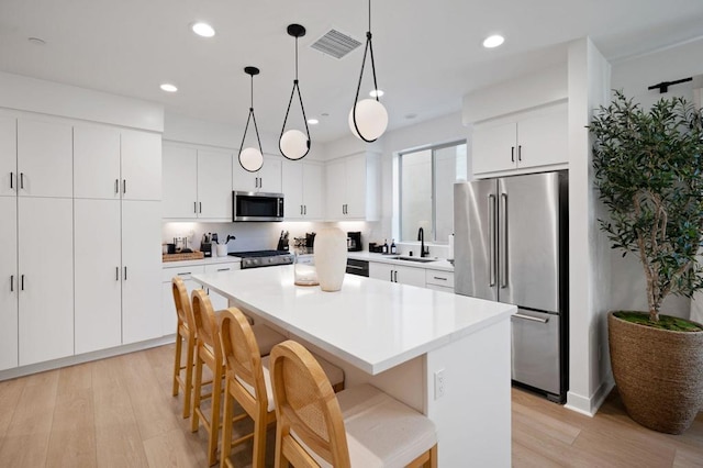 kitchen featuring sink, decorative light fixtures, a center island, stainless steel appliances, and white cabinets