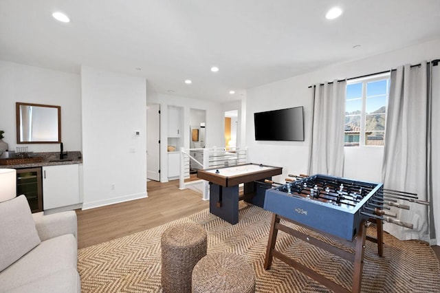 recreation room with bar, beverage cooler, and light hardwood / wood-style floors