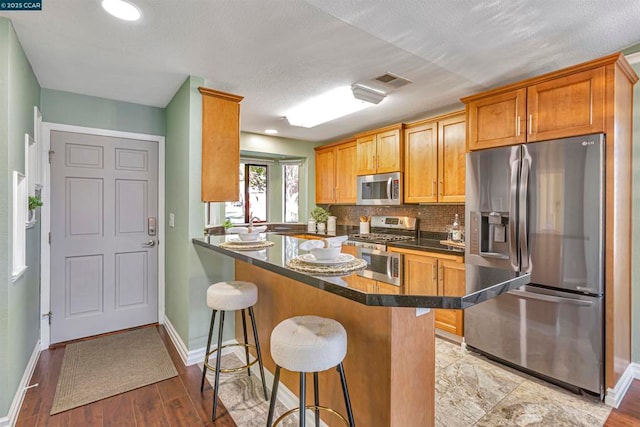 kitchen with tasteful backsplash, appliances with stainless steel finishes, a breakfast bar area, and kitchen peninsula