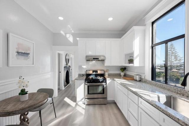 kitchen featuring stacked washing maching and dryer, stainless steel range with gas stovetop, light stone countertops, white cabinets, and light wood-type flooring