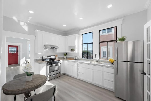 kitchen with appliances with stainless steel finishes, white cabinetry, light stone counters, crown molding, and light wood-type flooring