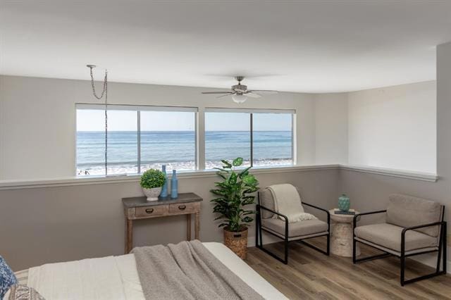 bedroom with hardwood / wood-style floors, ceiling fan, and a water view