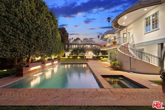 pool at dusk featuring an in ground hot tub and a patio area