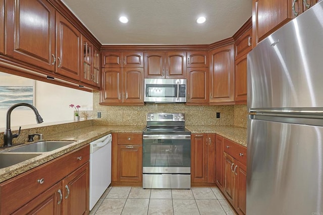 kitchen with sink, light tile patterned floors, appliances with stainless steel finishes, light stone countertops, and decorative backsplash