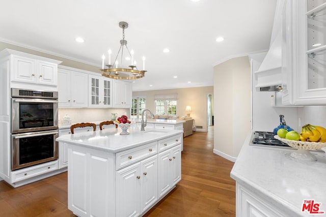 kitchen with sink, hanging light fixtures, a center island with sink, stainless steel appliances, and white cabinets