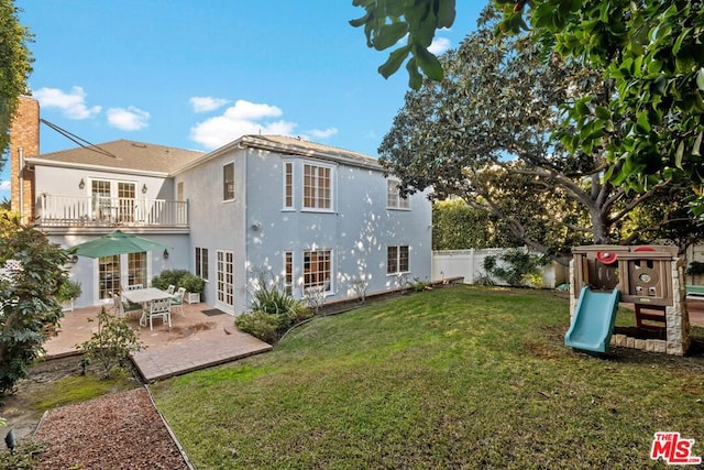 back of house featuring a playground, a balcony, a yard, a patio area, and french doors