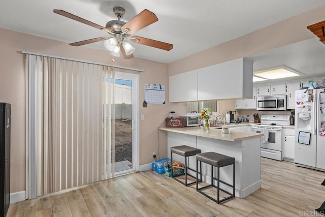 kitchen with a breakfast bar area, white cabinets, white appliances, kitchen peninsula, and light wood-type flooring