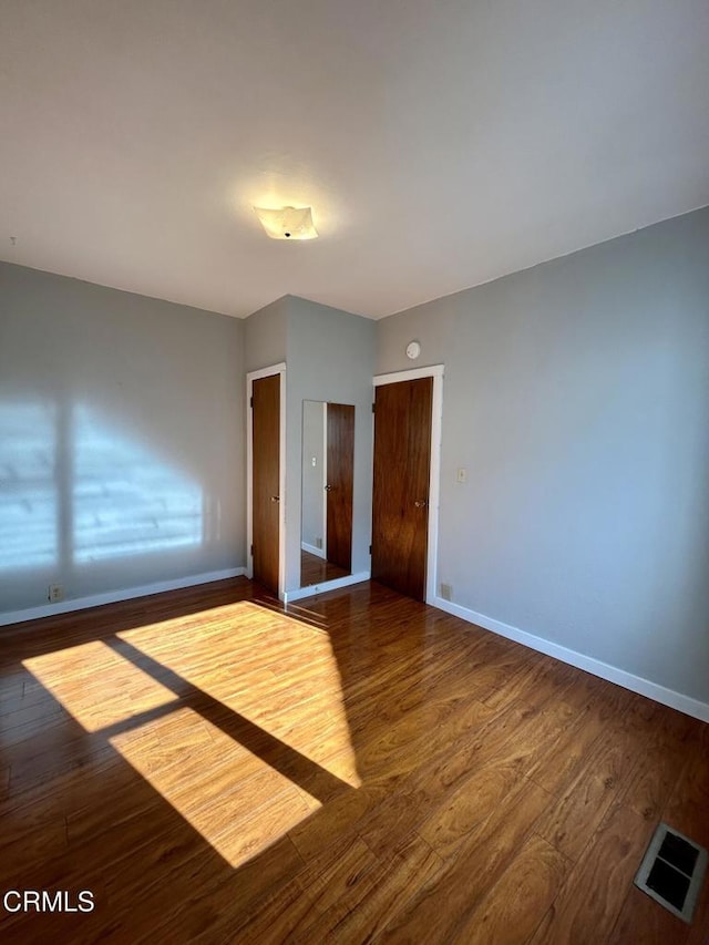 unfurnished bedroom featuring wood-type flooring, visible vents, and baseboards