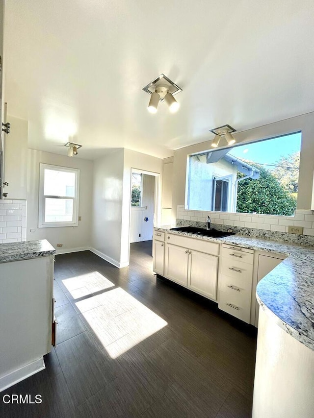 kitchen with baseboards, decorative backsplash, light stone counters, white cabinetry, and a sink