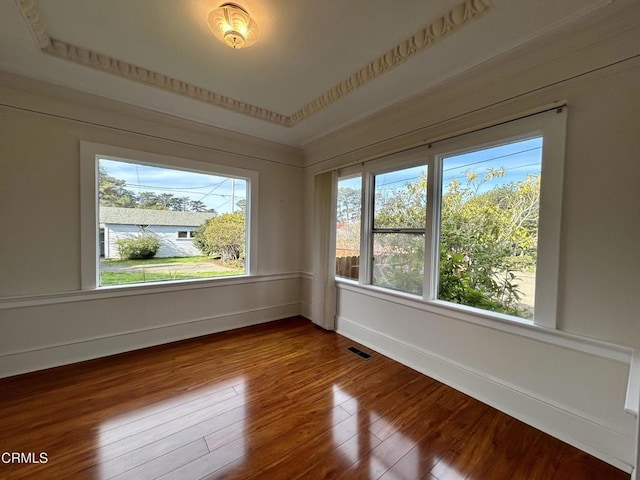 unfurnished room featuring a wealth of natural light, baseboards, visible vents, and hardwood / wood-style floors