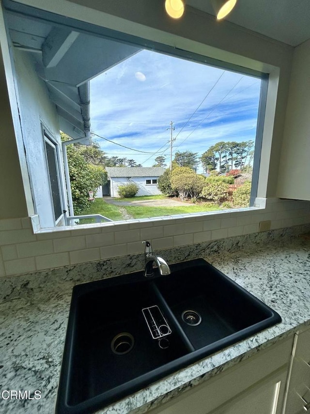 interior details featuring tasteful backsplash, white cabinets, a sink, and light stone counters