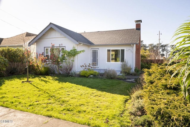 view of front of house with roof with shingles, a chimney, a front yard, and fence