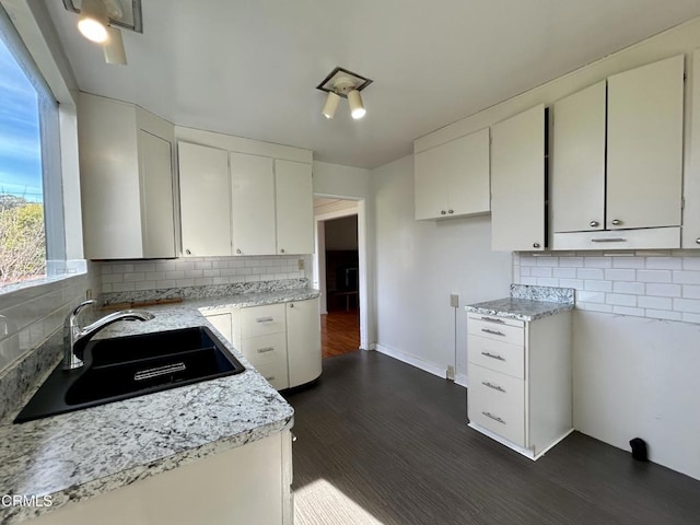 kitchen featuring dark wood-style floors, decorative backsplash, white cabinetry, a sink, and baseboards